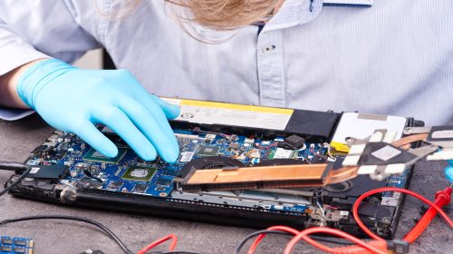 Hands of a technician repairing a broken laptop computer